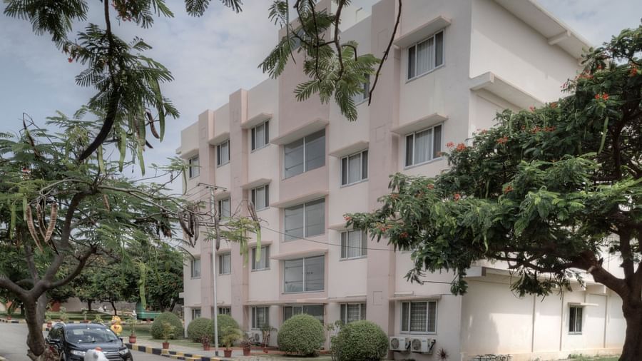 A street view of a modern white hotel building amidst lush greenery at Greens Inn - Cozy Accommodations in Hyderabad.