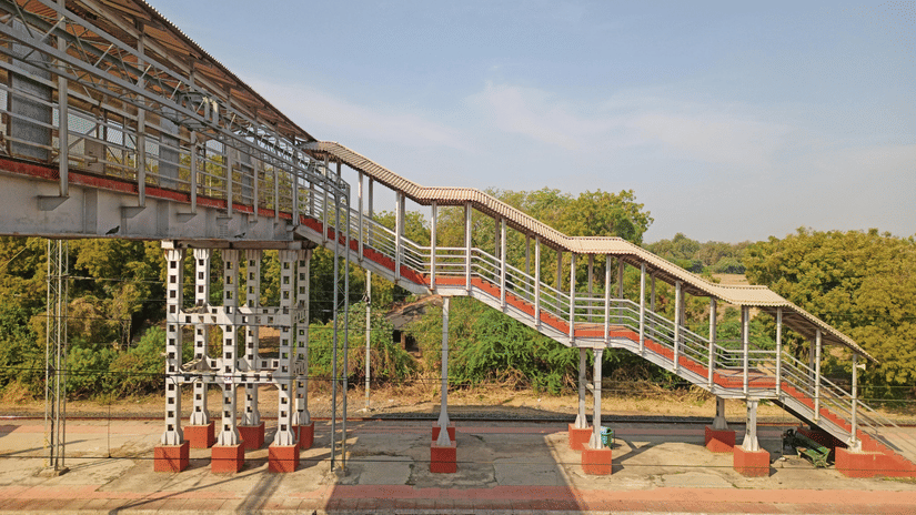 A foot overbridge at a railway station features stairs and a metal structure.