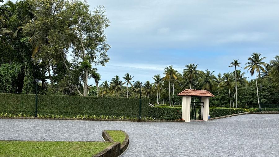 An entrance with  a patches of grass on the side and a backdrop of blue sky with periodic clouds at Still Waters, Varkala.