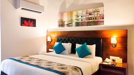 A spacious hotel room with a large bed, accent pillows, and a patterned runner. - Bamboo Saa Resort & Spa, Udaipur
