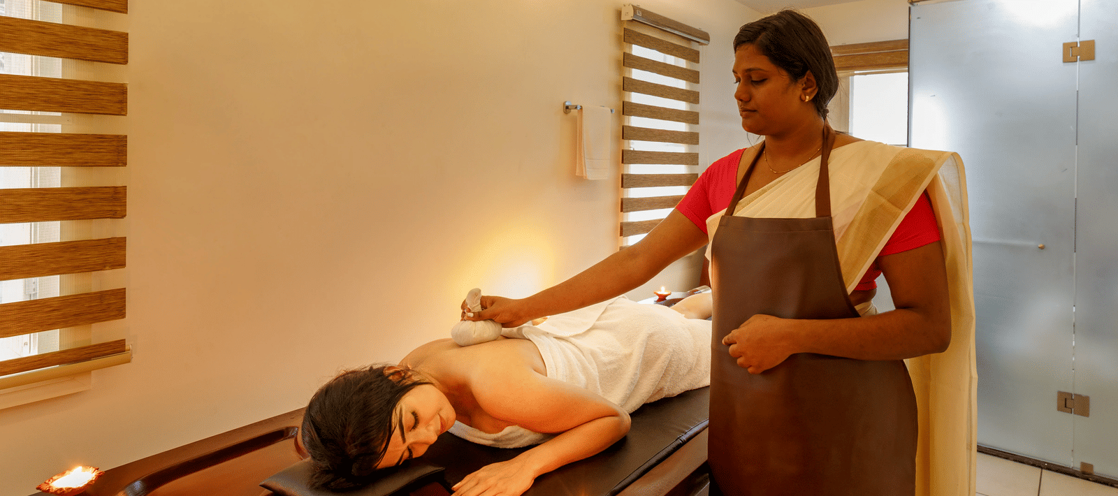 A person receiving a massage treatment on a wooden table in a softly lit room with brick accents.