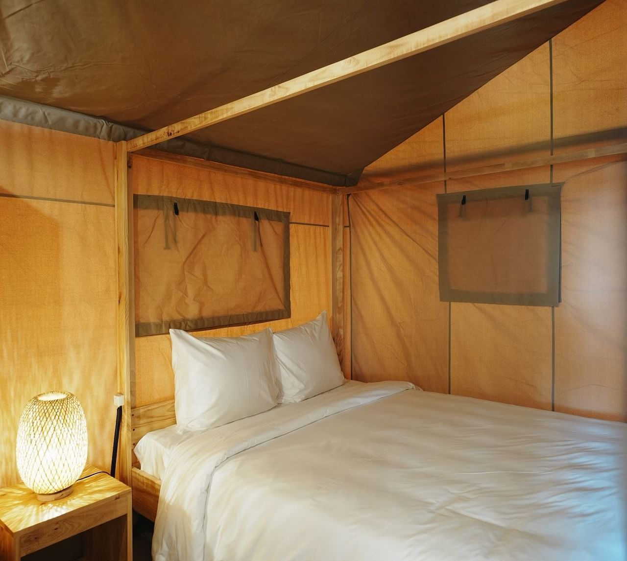 Inside the Peaceful Tent at WoCAL Retreat Ke Ga, a bedroom setup includes a neatly made bed and warm lighting, with wooden paneling creating a cocoon of comfort and calm.