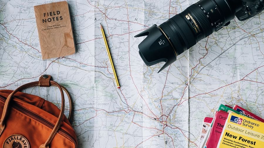 DSLR camera, notebook, pen, and a bag arranged aesthetically on a map.