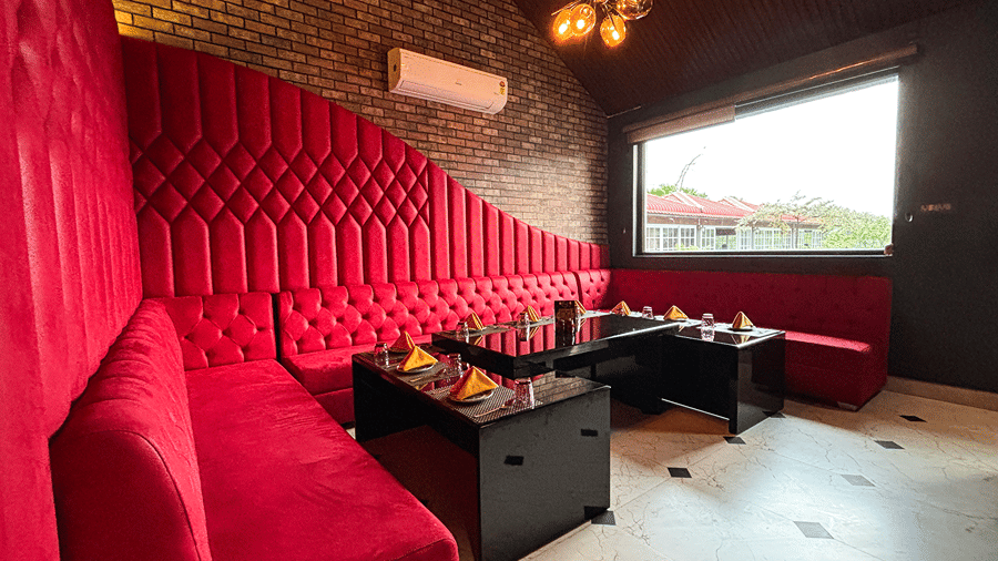 Private dining room with red tufted booth seating, black tables laid with napkins, a brick wall and a sputnik chandelier at HM Hotel & Resort, Dibrugarh.