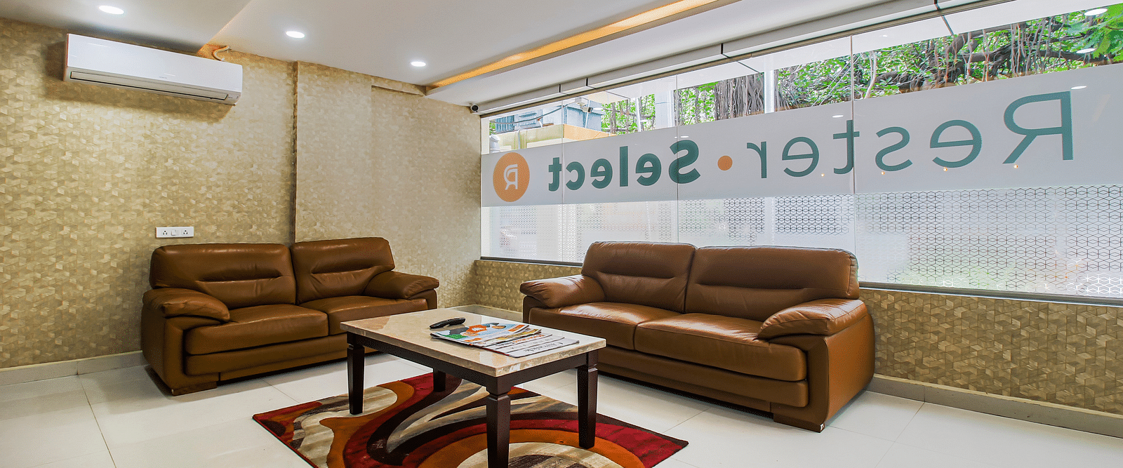 A waiting area with a comfortable brown leather sofa set, a patterned rug, and a glass partition with hotel branding.