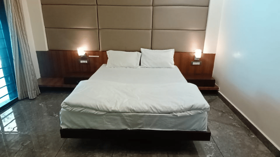 A close-up of a hotel room, focusing on a bed with a white duvet set against a wood-panelled headboard | Nandan Resort
