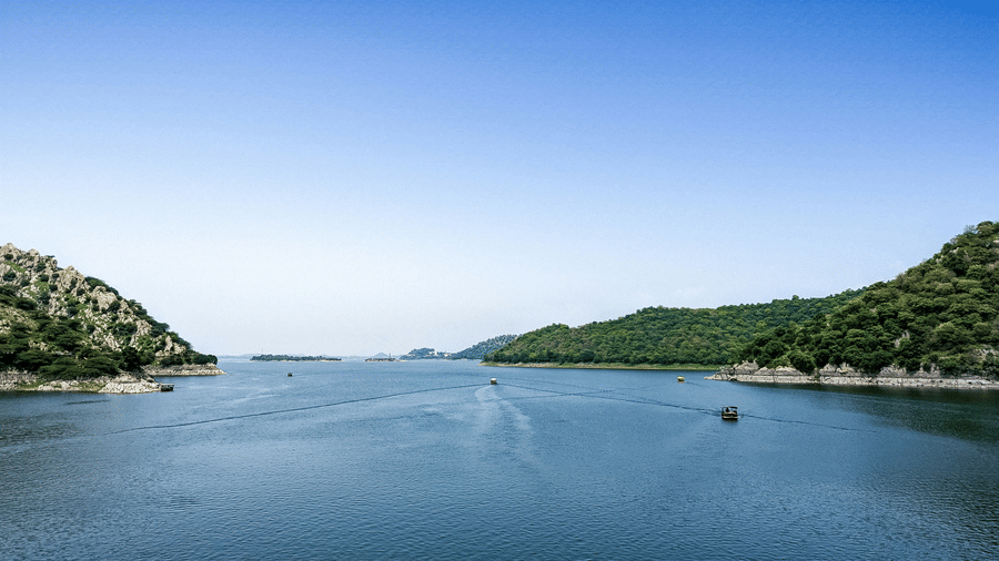 Expansive Jaisamand Lake, Alwar, under a clear blue sky with a few boats on the water