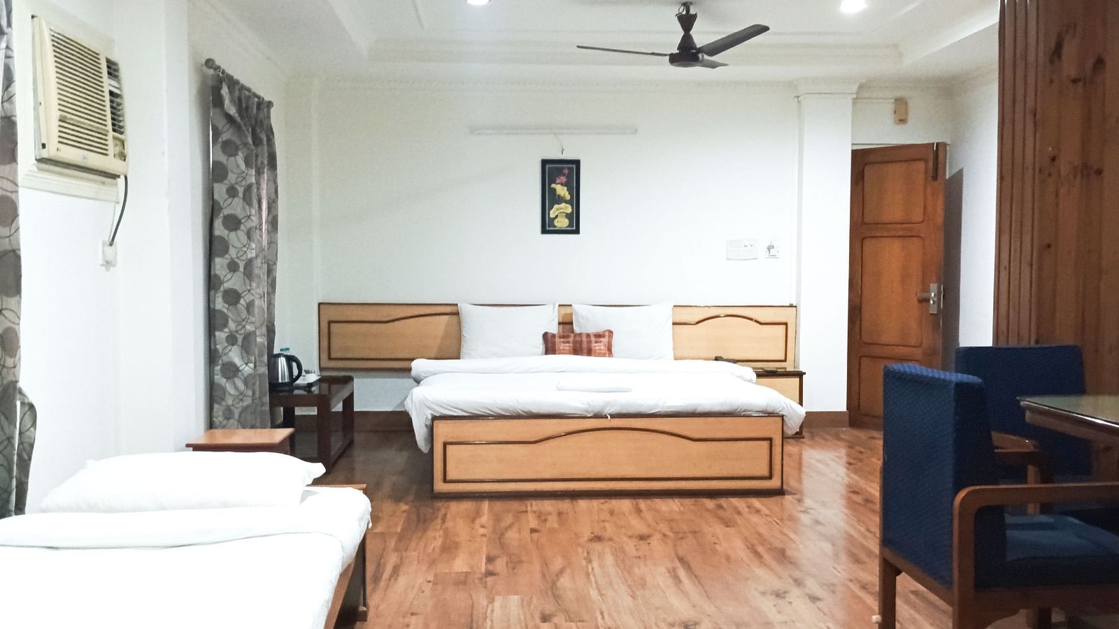 Spacious Deluxe Triple Room A.C. at Ecotel Vinayak, Siliguri featuring multiple beds, wooden flooring, and cosy seating.