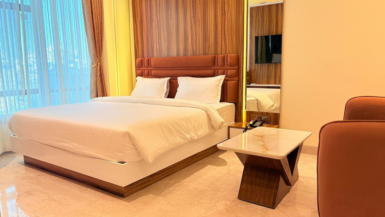 A bed with a wooden headboard and a television reflected in the mirror at Hotel Mumbai House, Vashi.