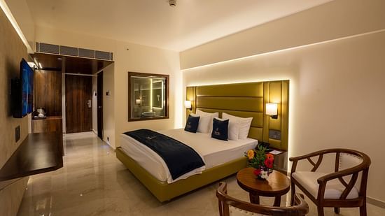 Side view of Deluxe King with plush bed and bedside tables seating area TV set coffee and tea maker and partial view of the washroom - Mastiff Grand - The Sia Palace Suites Banquets Khopoli
