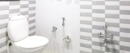 A brightly lit interior of a modern bathroom at Pravasa Ahmedabad featuring a commode along with the shower area beside it.