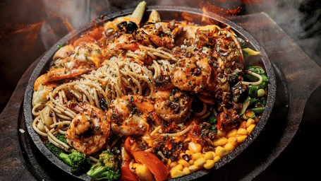The dish features a variety of meats and vegetables served on a cast-iron plate.