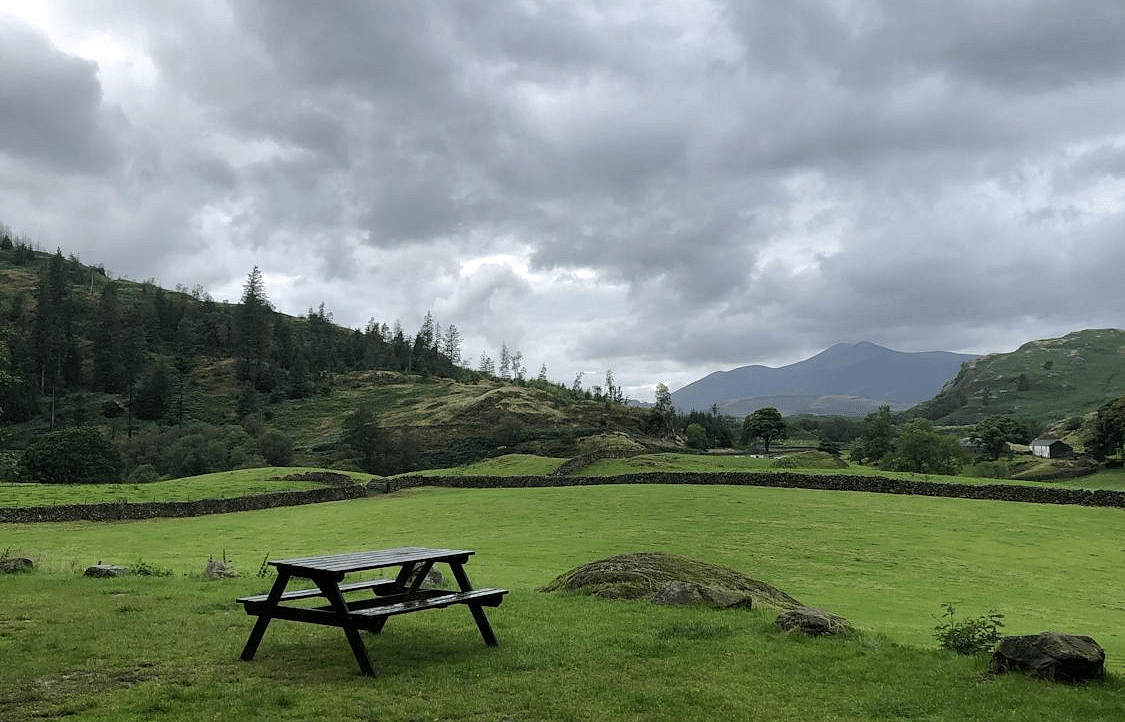 A beautiful mountain under a clear sky, with a table and attached seating set up on a green lawn, with a few houses in the vicinity