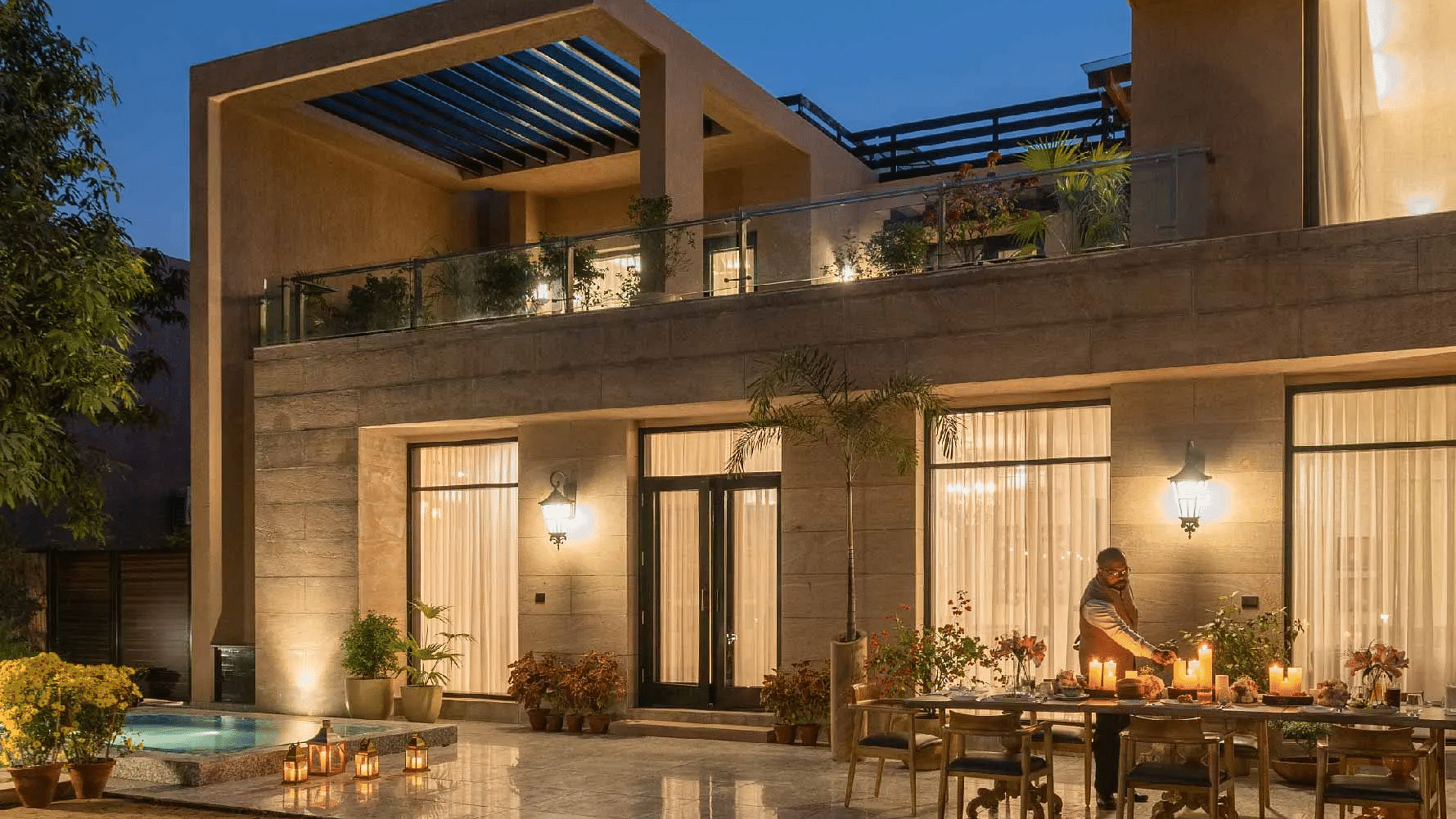 Modern two-storey house lit warmly at night, with large glass doors and an outdoor dining space at Karma Chalets.