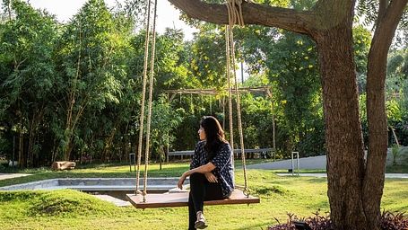 Guest sitting on a swing under a tree in the garden area at Karma Chalets.