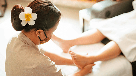 Spa therapist giving a leg massage to a client lying on a white massage bed with wooden shelves in the background at Karma Chalets.