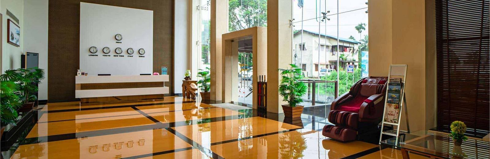 A brightly lit hotel lobby at Mansha Hotel Regency with shiny floors, a reception desk, and large glass windows looking out onto the exterior.