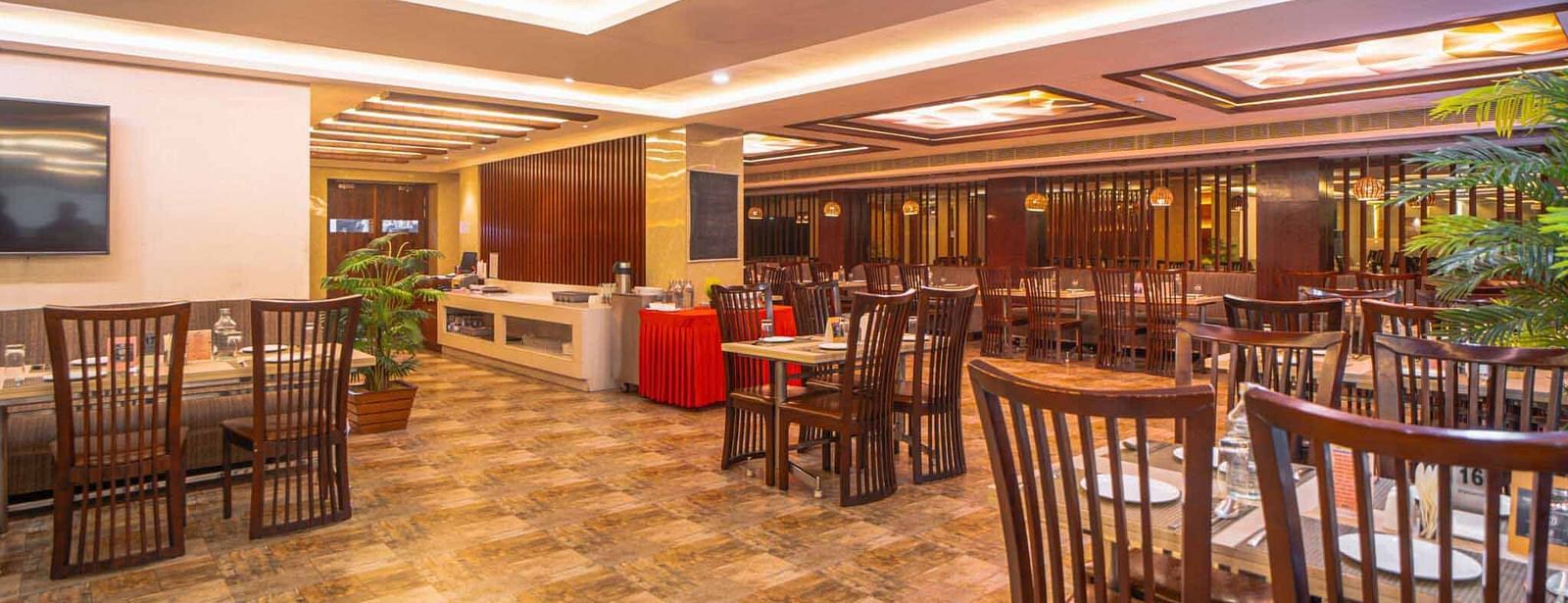 A wide shot of a spacious dining area with wooden tables and chairs, illuminated by warm ceiling lights at Mansha Hotel Regency.