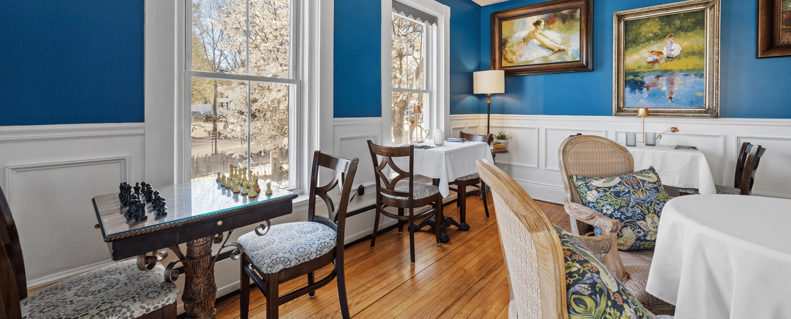 Dinning room  at Hartstone Inn with blue walls, white wainscoting, and large windows, furnished with antique-style chairs and tables.