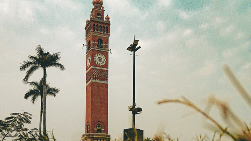 A tall, colonial-era clock tower stands in a grassy field against a hazy sky.