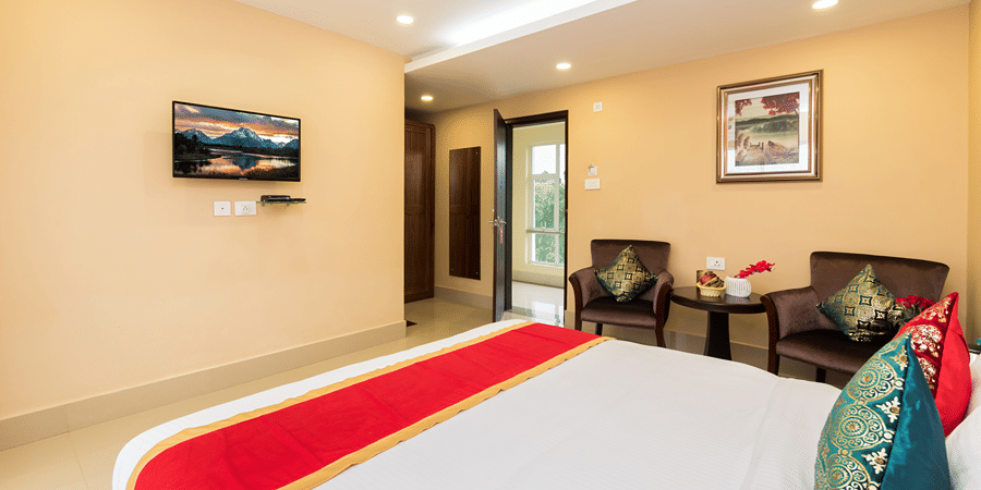 A bedroom featuring a bed with cushions and bed runner facing the TV mounted on the wall at Central Courtyard Boutique Hotel, Siliguri