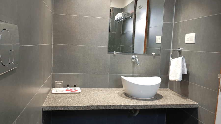 A bathroom vanity area at Hotel Ashray Inn Express showcasing a countertop wash basin, mirror, towel rail, and sleek finishes.