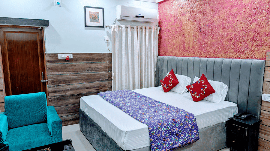 A cosy resort bedroom with a large bed, red accent cushions, a blue armchair, and a textured pink feature wall.