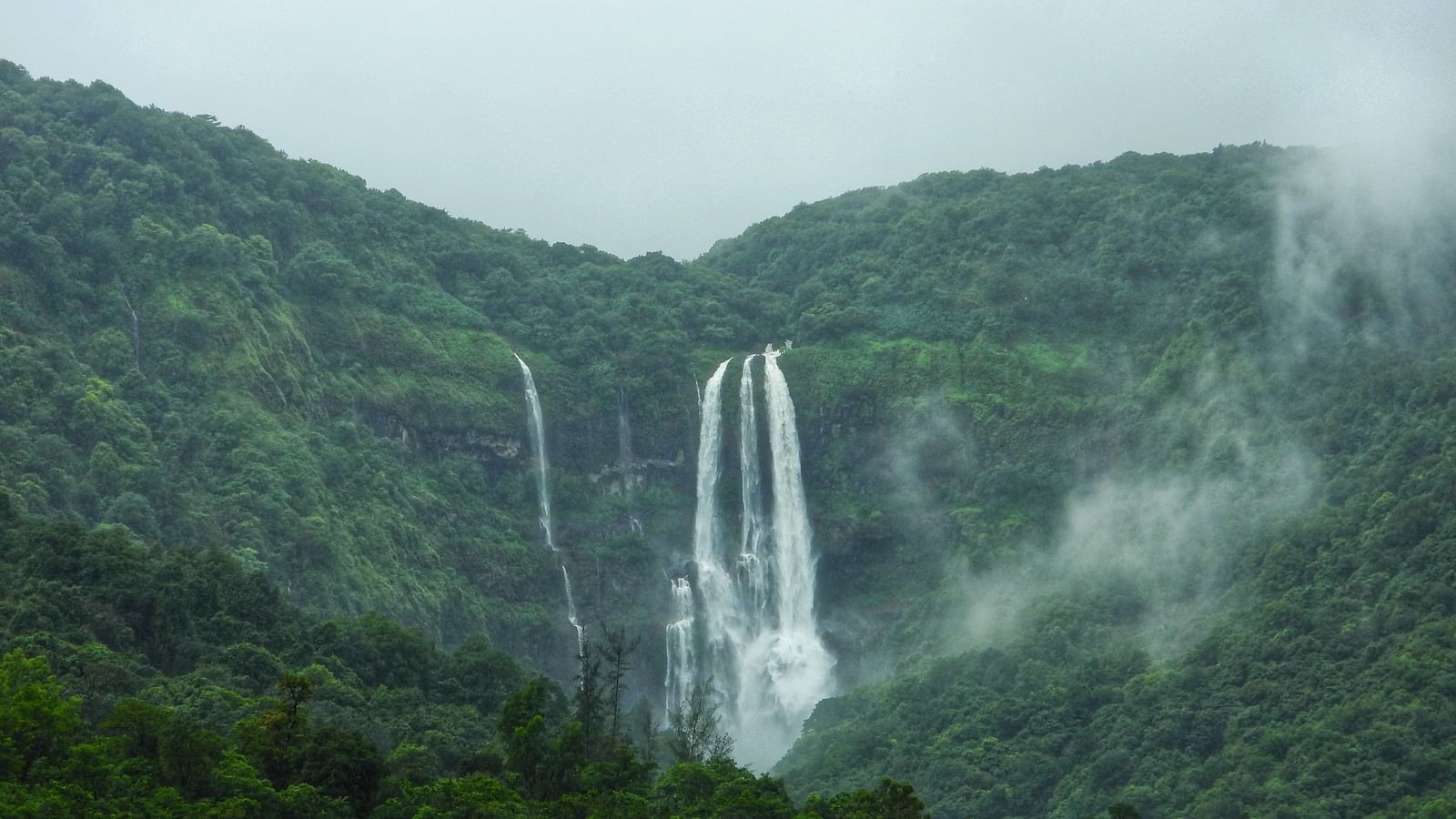 A majestic waterfall cascading down a green mountain covered in mist
