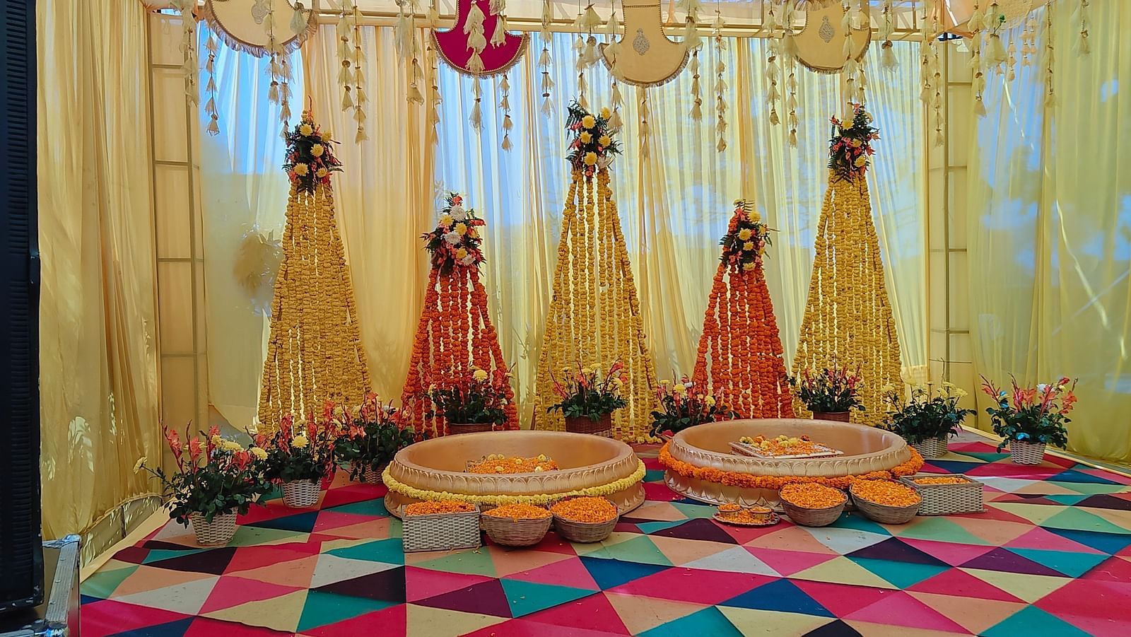 A beautifully decorated mandap with bright yellow drapes, colourful flooring, and traditional seating for ceremonies. | Brij Eternity, Vrindava