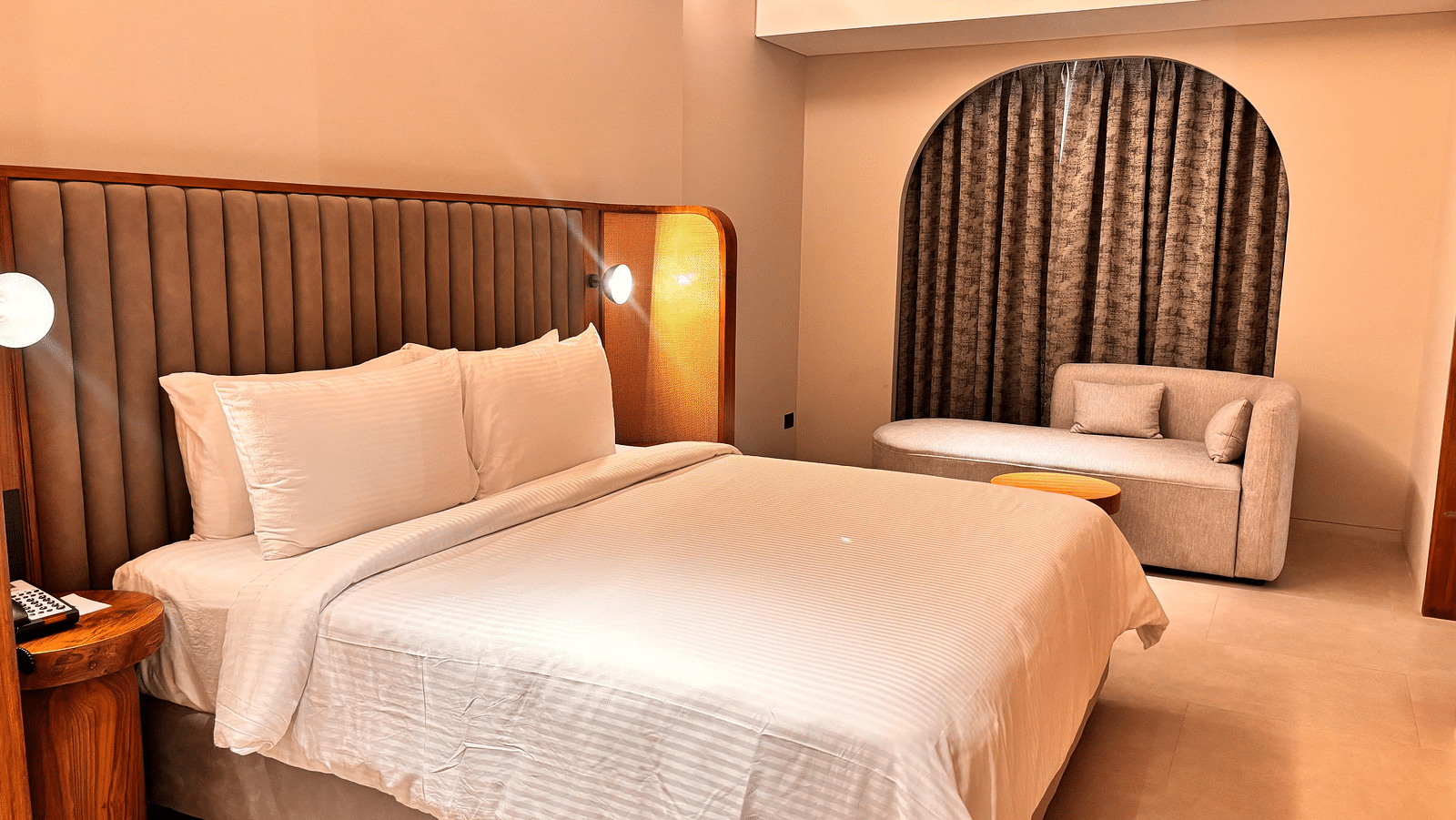 A bedroom at Swosti Premium Beach Resorts, Puri, with a made bed and an arched doorway leading to another room.