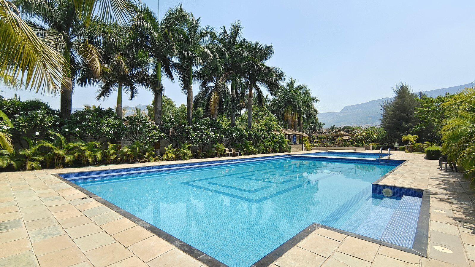 Swimming pool with blue water at The Kanila Resort surrounded by trees.
