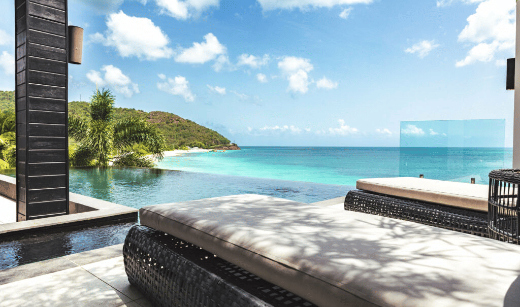 A luxurious outdoor lounge area with comfortable seating offers panoramic views of a stunning bay with clear blue water and green islands.