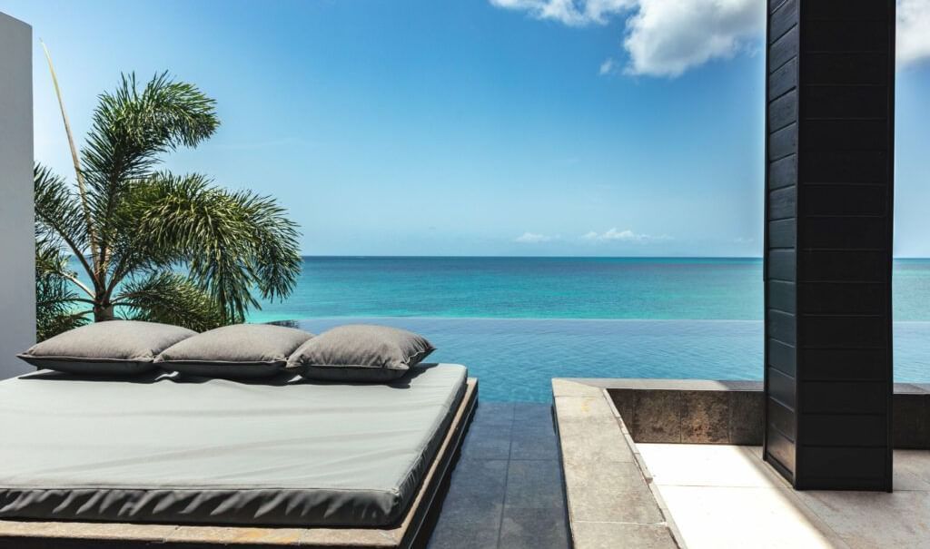 Modern lounge with a cushioned daybed overlooking a calm, turquoise ocean under a bright blue sky.