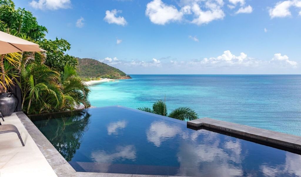 An infinity pool overlooking turquoise waters and lush greenery, offering a serene and luxurious tropical escape - Tamarind Hills Resort and Villas - Antigua