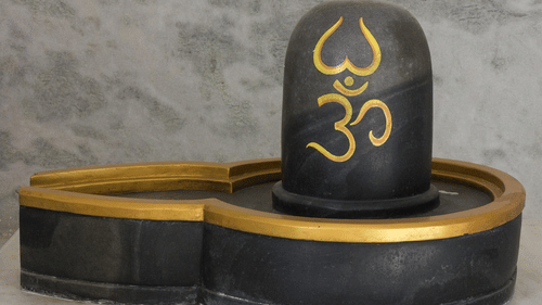 A Shiva lingam placed on a black base with the Om symbol written on it against a plain background.