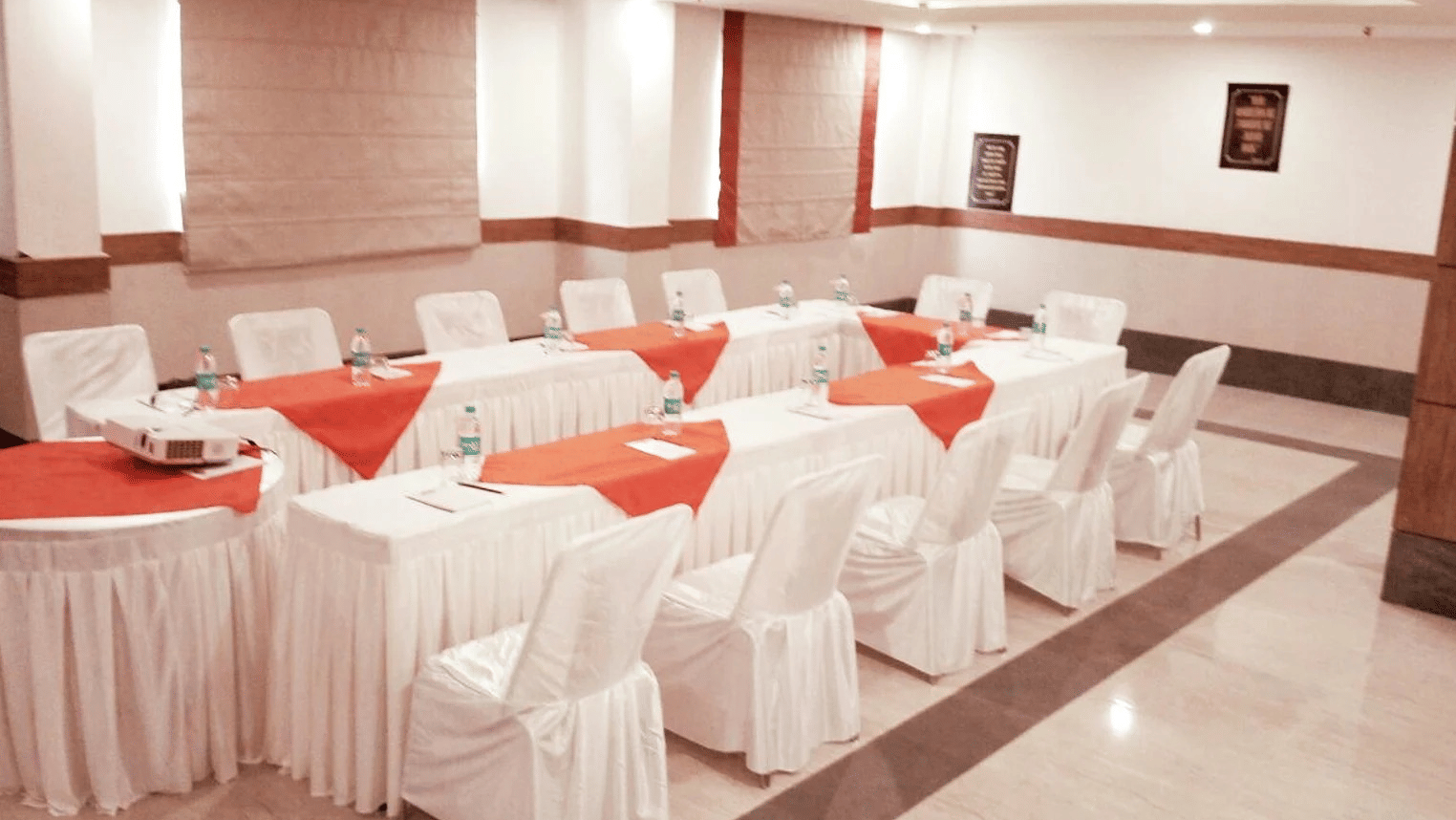 Elegant conference room setup with white-draped chairs and tables arranged in a U-shape for a business meeting.