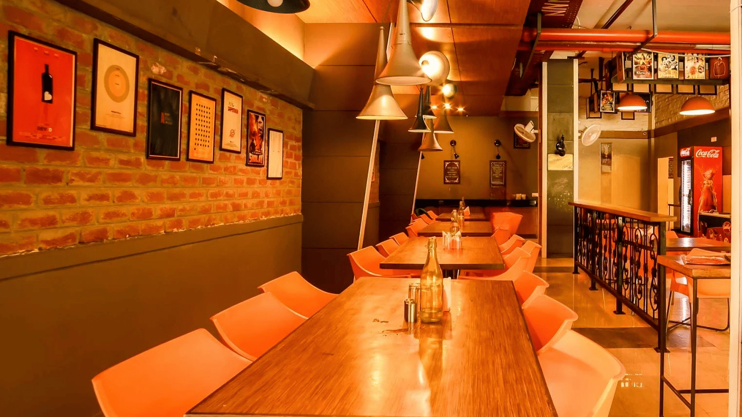 Cozy cafe interior with warm lighting, wooden tables, and modern decor featuring framed artwork on exposed brick walls.