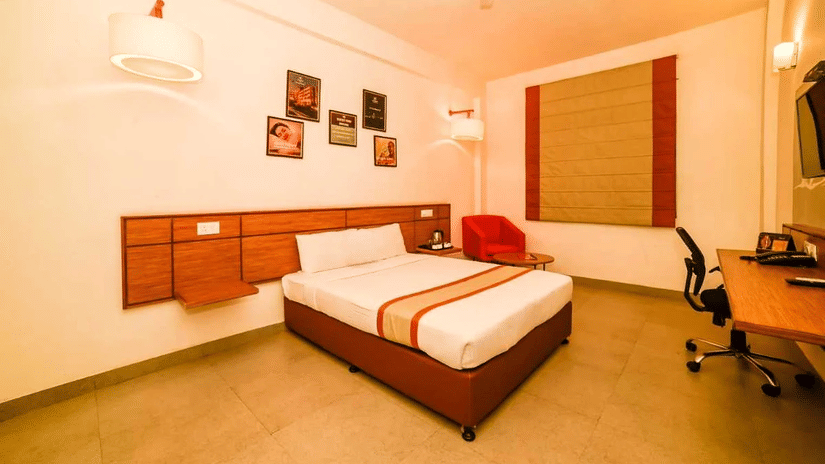 A hotel room featuring a single bed with a large mural of a cityscape, a working area with an ergonomic chair, and a warm color scheme.