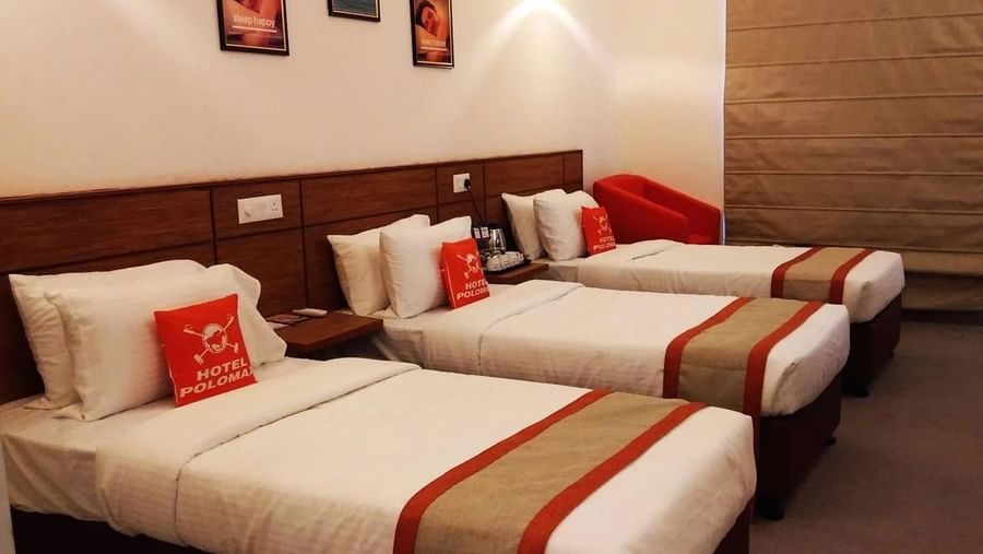 An image of a bedroom with three similar looking beds - An image of a reception lobby featuring a reception desk , and a seating area for the guest - Max Hotel Jabalpur