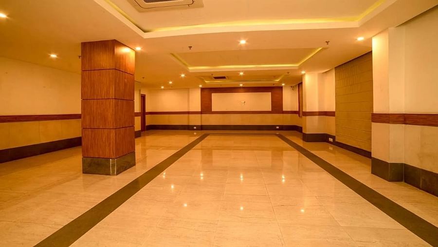 An image of a spacious banquet hall with installed lights in the ceiling - An image of a reception lobby featuring a reception desk , and a seating area for the guest - Max Hotel Prayagraj
