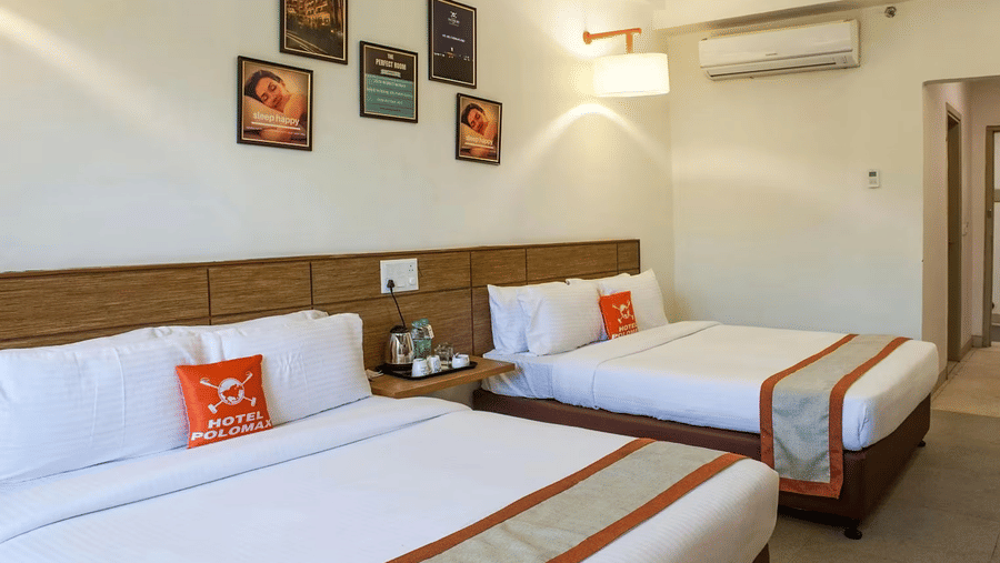 A hotel room with two single beds, adorned with white linens and orange accents, with framed pictures and amenities indicating a comfortable stay.