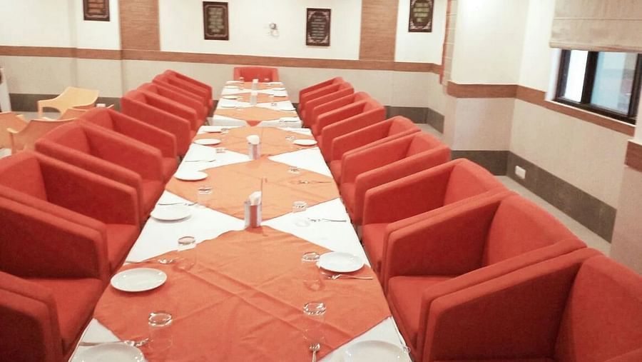 a long table featured in a spacious hall with big cushioned chairs around it - Max Hotel, Jabalpur