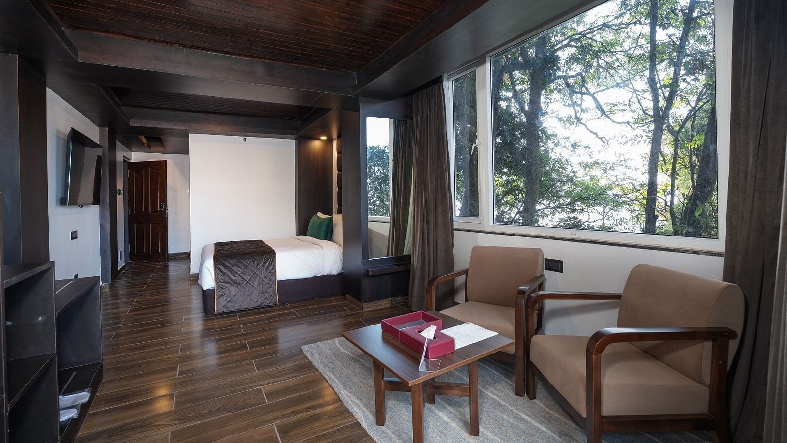 A sweeping shot of the room, showcasing the bed, cosy seating area with two chairs, and a table beside a grand window.