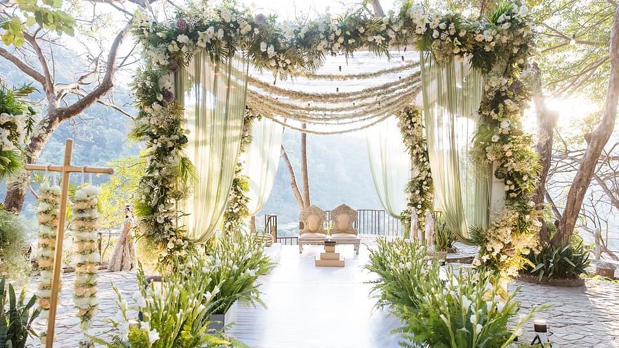 Stunning wedding mandap with white drapes, vibrant greenery, and a scenic backdrop of nature and sunlight