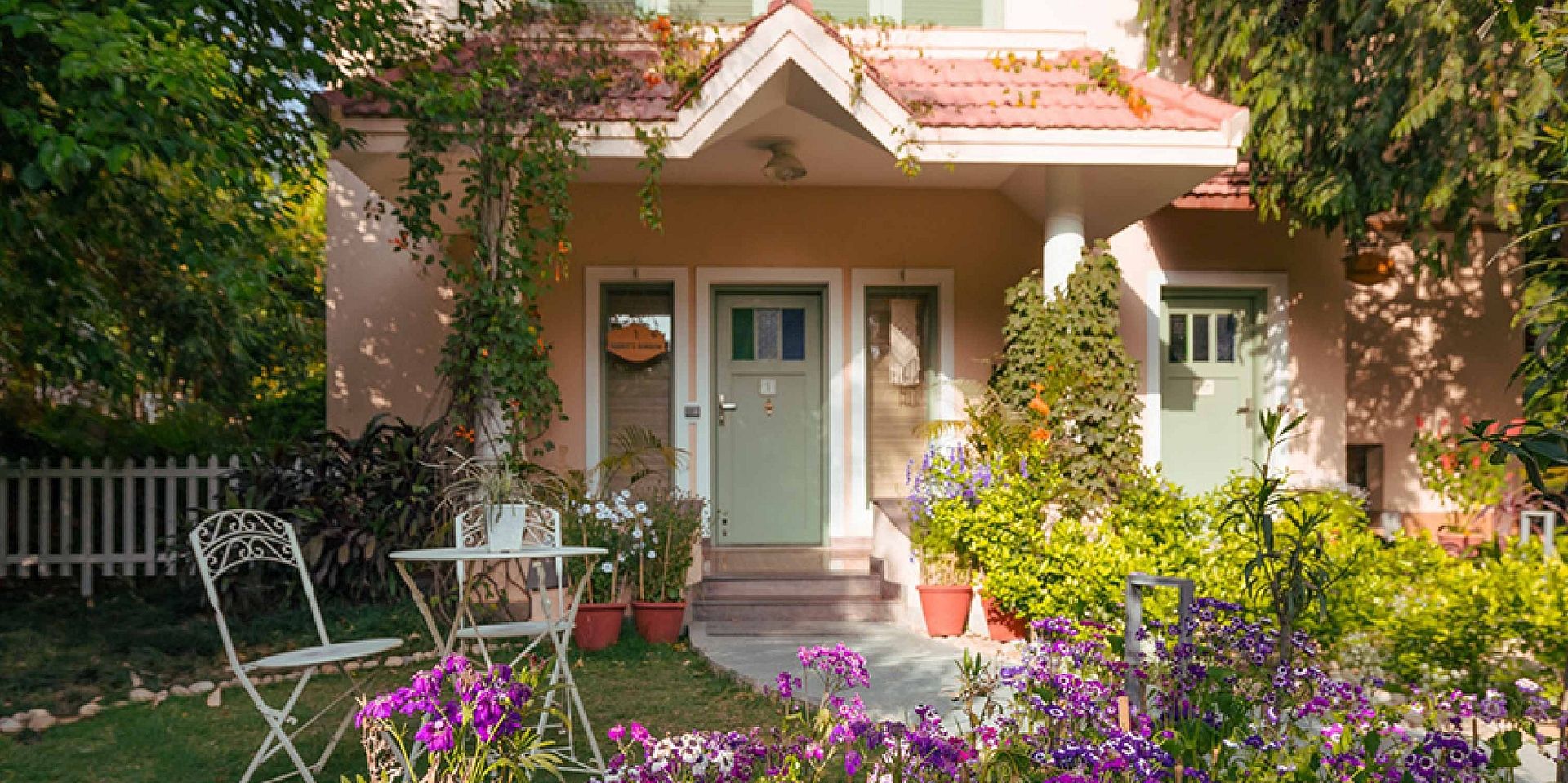 Rabbit Burrow at Karma Chalets with a small garden, outdoor chairs, flowers, and a white door with windows.