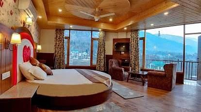 A spacious and luxurious hotel room with a round bed, plush seating, a balcony overlooking a scenic view, and elegant decor | DLS La Serene Manali