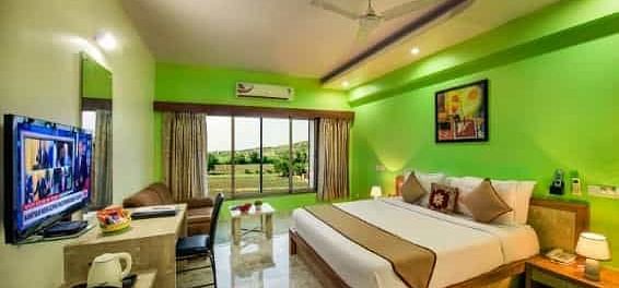 A brightly coloured room with a double bed, a television, and a balcony - Lion Lords Inn Rajula
