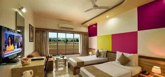 A modern room featuring twin beds with colourful wall panels and a television - Lion Lords Inn Rajula