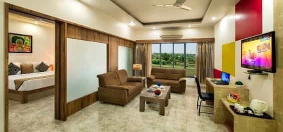 A spacious room including a seating area with sofas, a television, and large windows - Lion Lords Inn Rajula