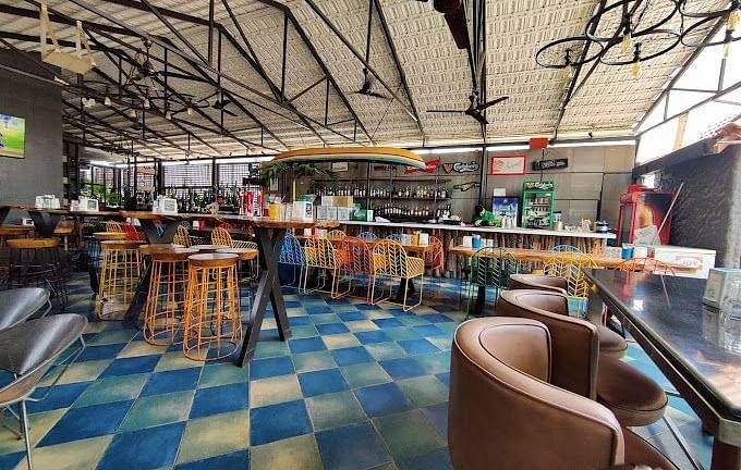 Spacious indoor restaurant with high ceilings, exposed beams, colorful chairs, and a checkered blue and white floor | Astra Hotels and Suites Kadubeesanahalli